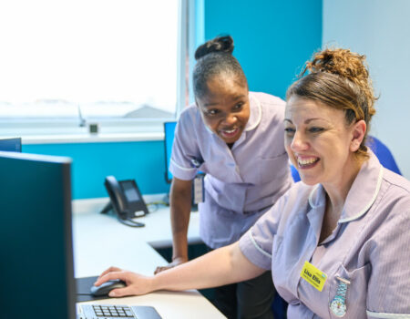Two healthcare support workers working on a computer smiling