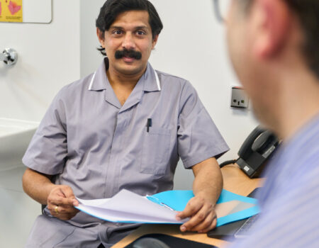 Healthcare support worker talking to a patient at a desk, with patient notes