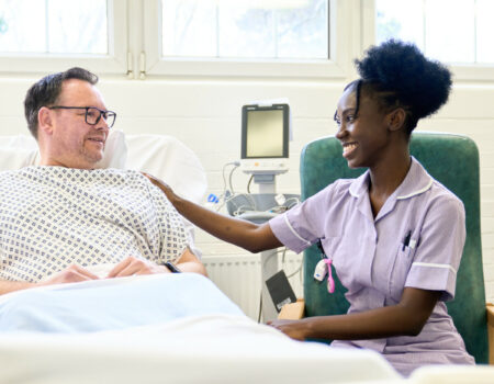 Healthcare support worker sitting next to patient in a bed smiling at each oter