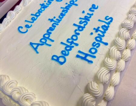 Large cake with writing stating 'celebrating apprenticeships Bedfordshire Hopsitals'